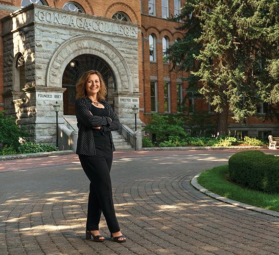 A man in commencement regalia holds up his degree with Gonzaga University written on it